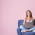 Dziewczyna siedząca na fotelu, trzymająca na kolanach laptopa. Siedzi na tle różowej ściany.